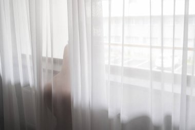 Büyük pencerenin yanında şeffaf perdenin arkasında çıplak güzel bir kadın duruyor..