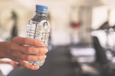 Kırpılmış. Spor malzemelerinin ve koşu simülatörlerinin karşısındaki spor salonunda elinde şişe suyu olan bir kız. Dinlenme zamanı. Sağlık kavramı.