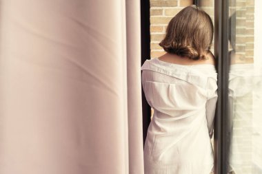 Şeffaf tişörtlü, pencereye yaslanmış, güzel, yalnız, üzgün, beyaz bir kadın..