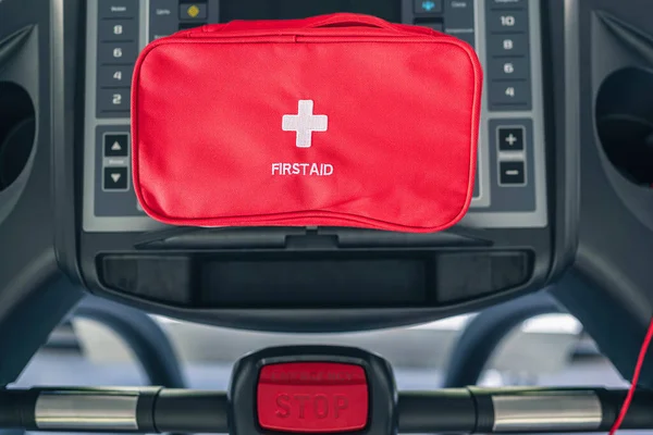 First aid kit red box in the fitness gym opposite the sport equipment and  jogging simulators. Healthy lifestyle, safety and help concept