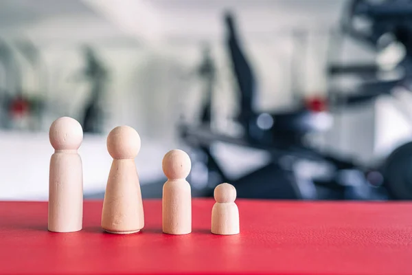 Wooden people family in the fitness gym opposite the sport equipment and  jogging simulators. Resting time. Health concept.