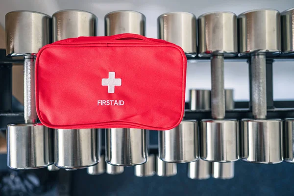 First aid kit red box on iron dumbbells in the fitness gym opposite the sport equipment and  jogging simulators. Healthy lifestyle, safety and help concept