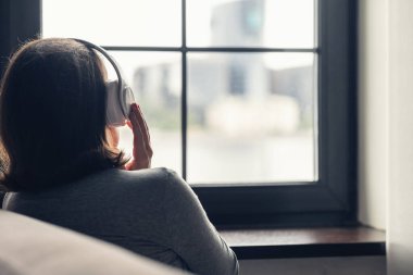 Kulaklıklı, apartman penceresinin yanında oturan ve müzik dinlemekten hoşlanan genç bir kadının arkası.. 