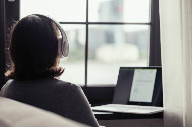 Yalnız bir kadının kulaklıkla müzik dinlemesi ve kafenin penceresinin yanında laptopla çalışması..