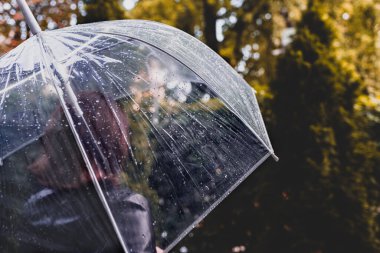 Sonbahar. Yalnız, üzgün, kızıl saçlı kadın parkta, bahçede yürüyor. Islak şeffaf şemsiyeden yağmur damlalarıyla bak. Yağmurlu bir manzara. Vintage Tone