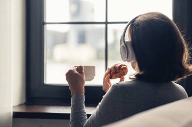 Soğuk kış sabahı pencerenin kenarında oturan ve kulaklıkla müzik dinleyen, bir fincan sıcak çikolata ve kruvasanla kahvaltı eden yalnız ve genç bir kadın.. 