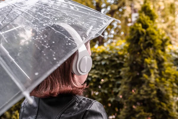 庭を歩いてヘッドフォンで孤独な悲しい赤毛の女性 雨滴とぬれた透明な傘を通して表示します 雨の日の風景 ヴィンテージトーン — ストック写真