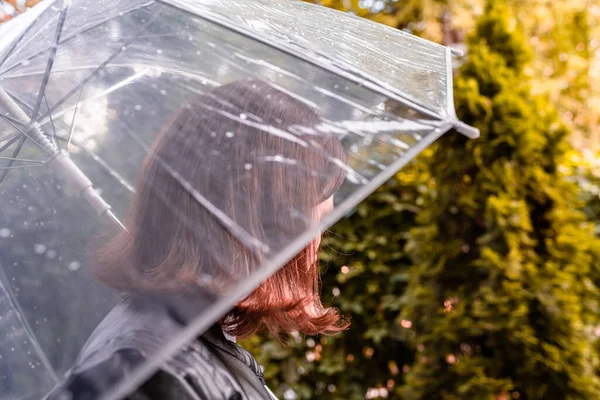 庭を歩く孤独な悲しい赤毛の女性 雨滴とぬれた透明な傘を通して表示します 雨の日の風景 — ストック写真