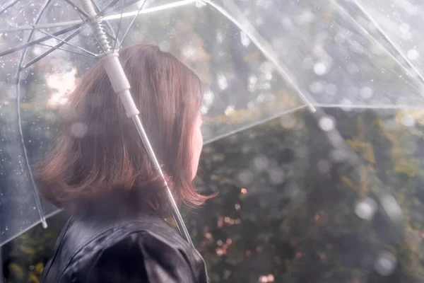 庭を歩く孤独な悲しい赤毛の女性 雨滴とぬれた透明な傘を通して表示します 雨の日の風景 ヴィンテージトーン — ストック写真
