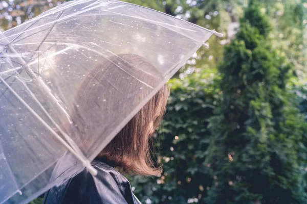 雨の透明な傘の下で孤独な赤毛の女の子が公園 庭を歩いて値下がりしました 雨の日の風景 — ストック写真