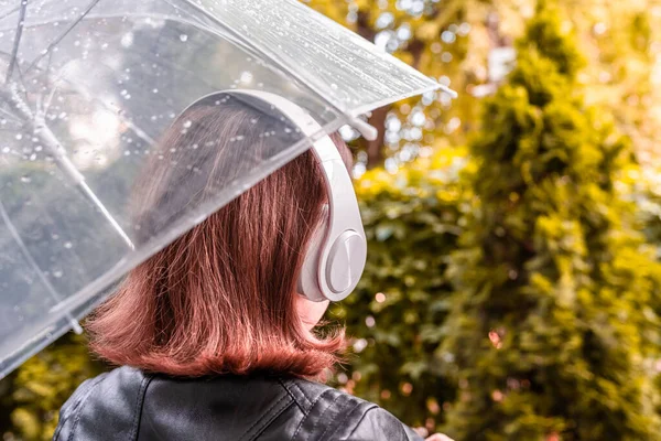 庭を歩いてヘッドフォンで孤独な悲しい赤毛の女性 雨滴とぬれた透明な傘を通して表示します 雨の日の風景 トーン — ストック写真