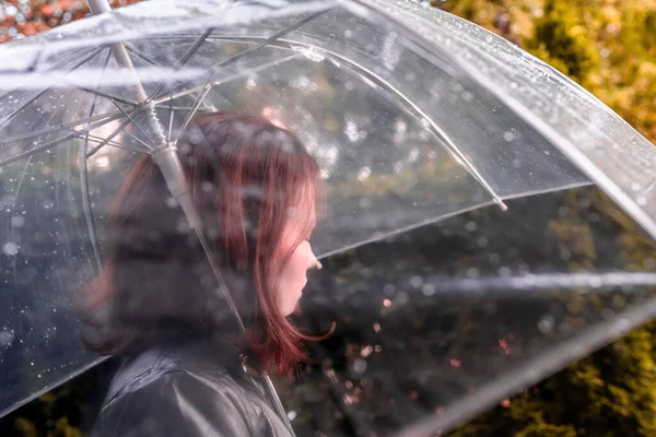 庭を歩く孤独な悲しい赤毛の女性 雨滴とぬれた透明な傘を通して表示します 雨の日の風景 ヴィンテージトーン — ストック写真