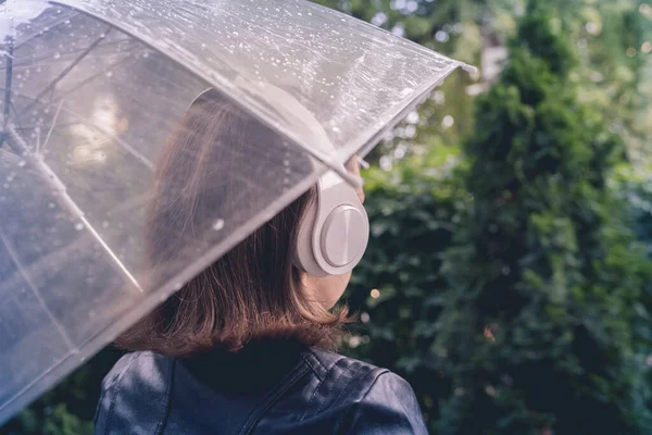 庭を歩いてヘッドフォンで孤独な悲しい女性 雨滴とぬれた透明な傘を通して表示します 雨の日の風景 ヴィンテージトーン — ストック写真