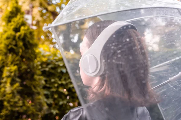 庭を歩いてヘッドフォンで孤独な悲しい女性 雨滴とぬれた透明な傘を通して表示します 雨の日の風景 — ストック写真