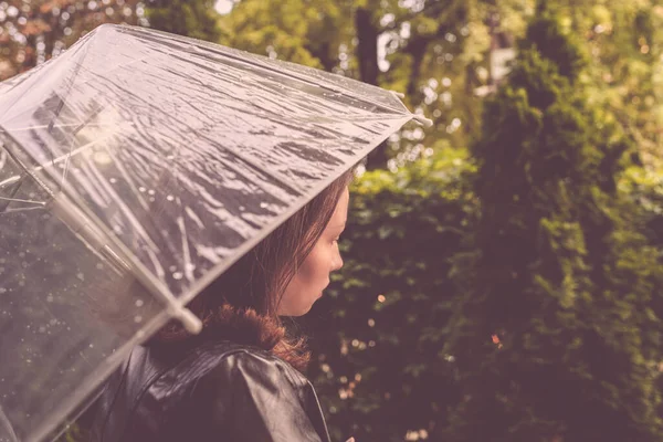 雨の透明な傘の下で孤独な赤毛の女の子が公園 庭を歩いて値下がりしました 雨の日の風景 ヴィンテージトーン — ストック写真