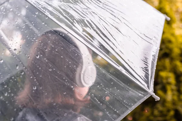 庭を歩いてヘッドフォンで孤独な悲しい女性 雨滴とぬれた透明な傘を通して表示します 雨の日の風景 ヴィンテージトーン — ストック写真