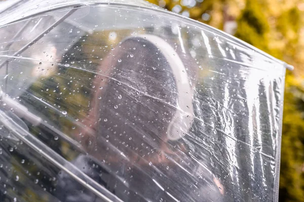 庭を歩いてヘッドフォンで孤独な悲しい女性 雨滴とぬれた透明な傘を通して表示します 雨の日の風景 ヴィンテージトーン — ストック写真