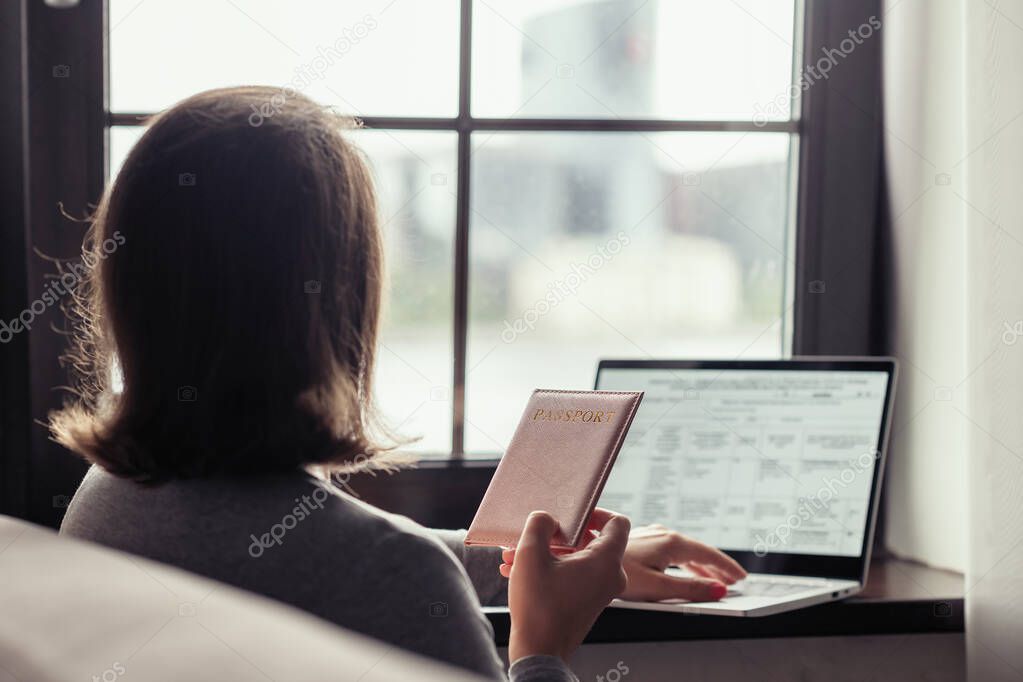 Woman  holding passport filling visa application form on the laptop. Online and home work concept.