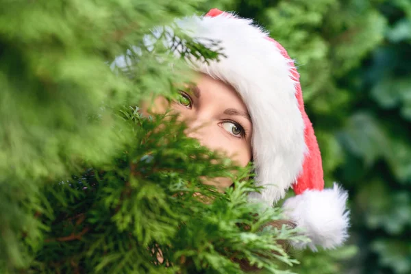 Девушка Красивыми Глазами Шляпе Санта Клауса Прячется Рождественской Ёлкой Концепция — стоковое фото