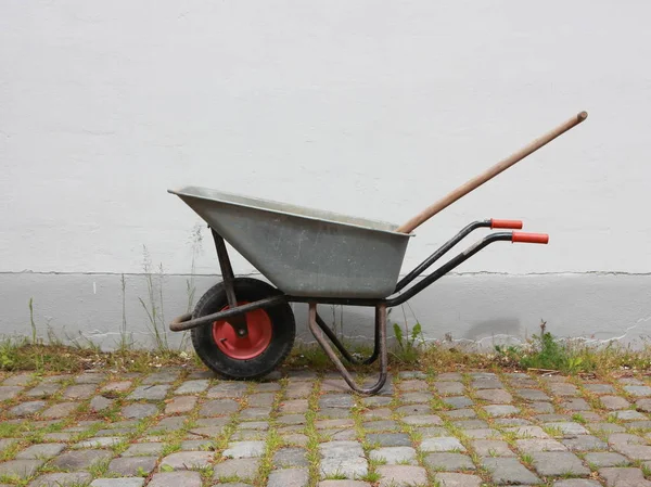 Carretilla de ruedas gris en la superficie de Cobble con hierba — Foto de Stock