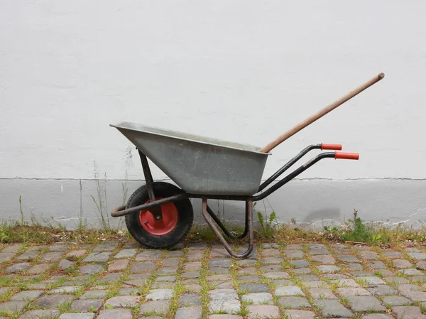 Graue Schubkarre auf Kopfsteinpflaster mit Unkraut — Stockfoto