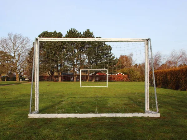 Arka planda evler olan çimenli bir arazide iki beyaz tahta kale direği. Bir kale direği diğerinin ağından görülür..