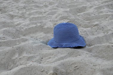 Bir kadının çizgili şapkası kumlu sahilde yatıyor. Arka planda kumdan yapılmış büyük bir Panama şapkası. Yaklaştın. Konsept: tatil, seyahat, yaz.