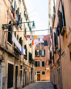 İtalya, Venedik 'te yüksek duvarlar arasındaki avluda çamaşır kurutma. Tipik bir Venedik cephesinde çamaşır asılıydı. Venedik 'te renkli binalar ve ipte kurumuş giysiler olan dar bir sokak.