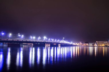 Riga, Letonya 'daki Taş Köprü manzarası. Akşamları Riga Stone Köprüsü. Aydınlatılmış yol ve Ulusal Kütüphane. 