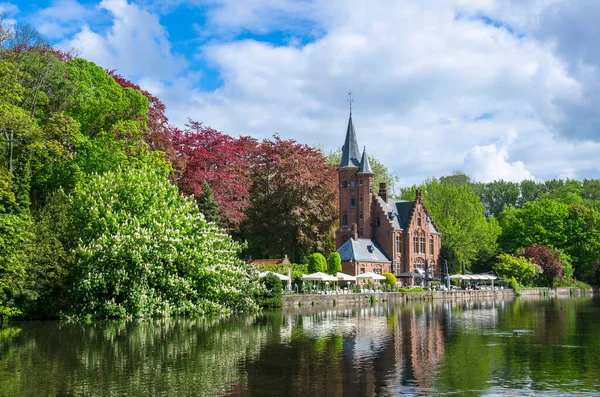 View of tranquil public green space featuring Minnewater Lake and small castle in Bruges during sunny day in spring, Belgium