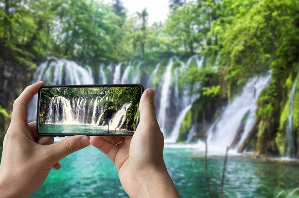 Tourist taking photo of waterfall with emerald water. Man holding phone and taking picture in Plitvice lakes national park, Croatia.