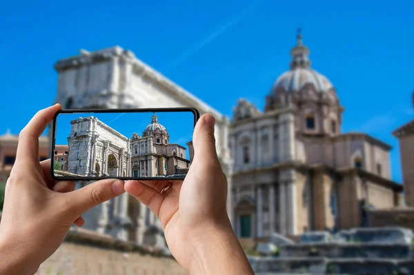 観光客は イタリアのローマのローマフォーラムで夏の日に古代遺跡の写真を撮る 男は電話を保持し 皇帝セプティミウスセヴェルスと教会サンルーカ マルティナの写真を撮る — ストック写真
