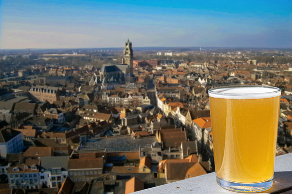 Glass of light Belgian beer with panoramic view from above of old town and big cathedral in Ghent, Belgium. View from above of Ghent, Belgium
