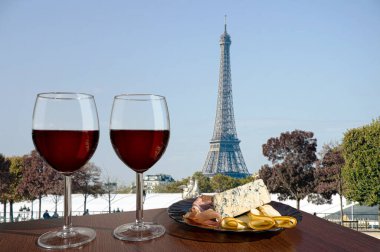 Paris ve Eyfel Kulesi manzaralı iki kadeh kırmızı şarap. Farklı atıştırmalıklarla bir bardak kırmızı şarap. Jambonlu, dilimlenmiş, mavi peynirli tabak. Romantik bir çift..