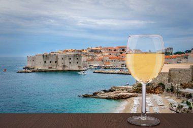 Dubrovnik arka planına karşı bir kadeh beyaz şarap. Tatil konsepti. Hırvatistan 'ın Dubrovnik kentinin tarihi merkezindeki sahil ve kent duvarı