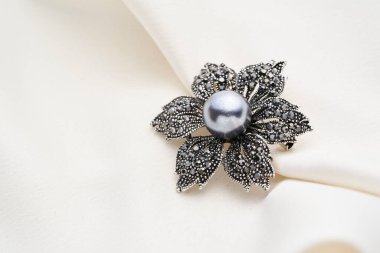 Çiçek şeklinde gümüş bir broş. Küçük elmaslar ve siyah inciler. Beyaz arka planda izole edilmiş.. 