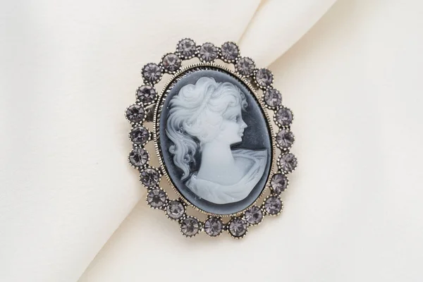 Broche Cameo, que é um retrato lateral de uma mulher, com pequenos cristais ao redor das bordas em um fundo branco . — Fotografia de Stock