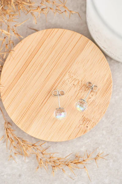 Close up stud earrings, with iridescent crystals. Beautiful earrings on wooden plate. Women accessories.