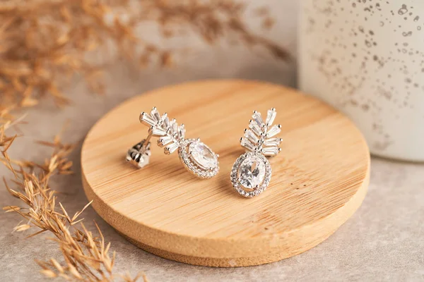 Close up silver stud earrings, with white crystals and diamonds. Beautiful earrings on wooden plate Women accessories.
