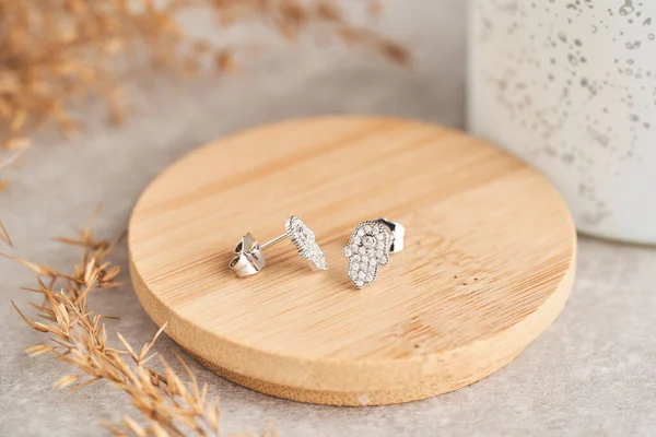 Close up golden stud earrings, with white crystals and diamonds in the form of a hamsa, a protective amulet. Beautiful earrings on wooden plate Women accessories.