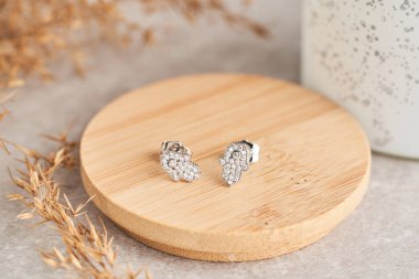 Beyaz kristaller ve elmaslarla kaplı altın küpeleri, koruyucu bir tılsım olan hamsa şeklinde kapatıyoruz. Tahta tabakta güzel küpeler Kadın aksesuarları.