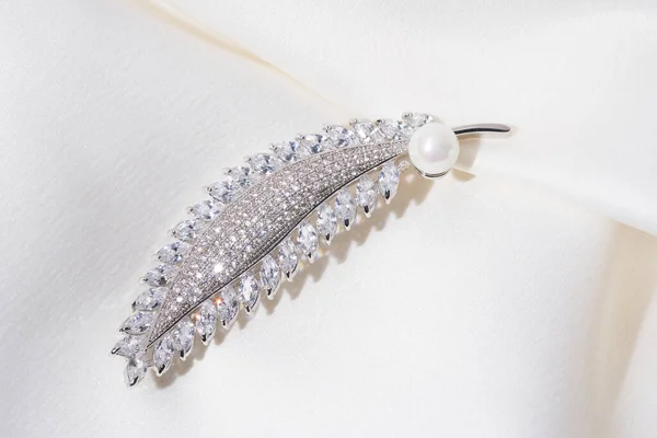Zilveren broche in de vorm van een veer, met kleine diamanten en witte parel geïsoleerd op een delicate achtergrond van veren. — Stockfoto