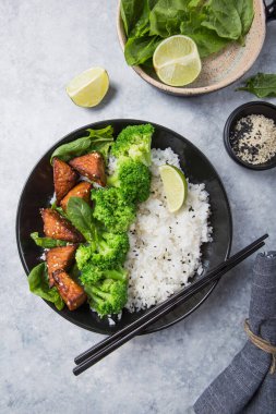 Vegan teryaki tempeh ya da tempe budha kasesi pilav, brokoli buğulama, ıspanak ve gri arka planda limon. Sağlıklı yemek.
