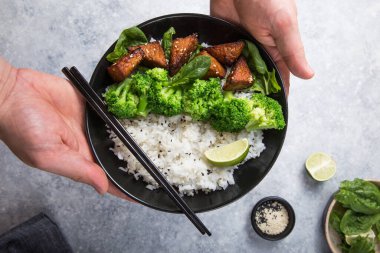 Vegan teryaki tempeh ya da tempe budha kasesi pilav, brokoli buğulama, ıspanak ve gri arka planda limon. Sağlıklı yemek.