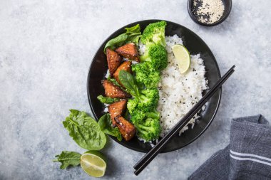 Vegan teryaki tempeh ya da tempe budha kasesi pilav, brokoli buğulama, ıspanak ve gri arka planda limon. Sağlıklı yemek.
