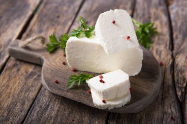 Suluguni peyniri ahşap bir tahtanın üzerinde büyük parçalara ayrılır. Maydanoz yaprakları ve biberle süslenmiş..