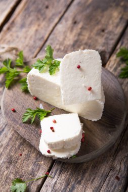 Suluguni peyniri ahşap bir tahtanın üzerinde büyük parçalara ayrılır. Maydanoz yaprakları ve biberle süslenmiş..