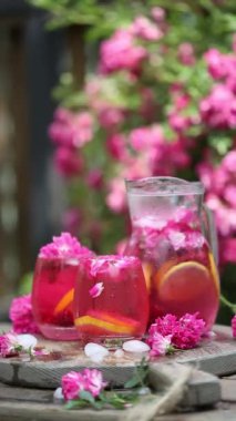 Buzlu gül limonatası ve doğal bahçenin üzerinde taze güller. Kız bir sürahide limonata dolduruyor.