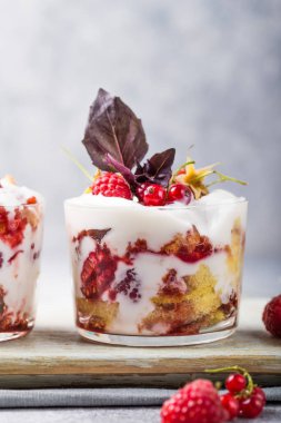 Hafif arka planda servis edilen bardaklarda sünger keki, krema ve ahududu ile katmanlı tatlı. Kopyalama alanı ile