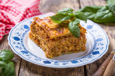 Tahta masadaki tabakta taze fesleğen ve parmesan peynirli et lazanyası. Kapat. İtalyan yemeği..
